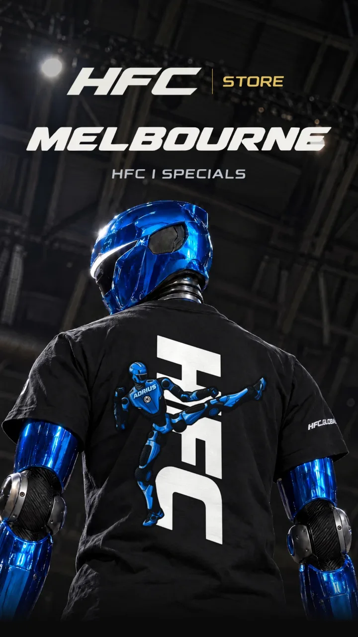 ADRIUS, a blue chrome HFC machine, seen from behind in a black HFC tee with the ADRIUS flying-kick print, under arena lights. HFC Store, Melbourne, HFC I specials.